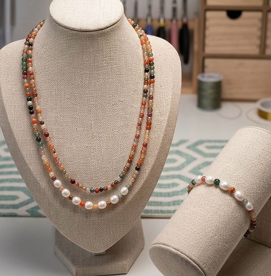 A pearl and agate necklace on a linen bust, with spools of thread and a wooden drawer chest behind it