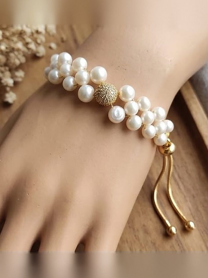Three strands of white pearls on a wrist, closed with a gold drawstring clasp
